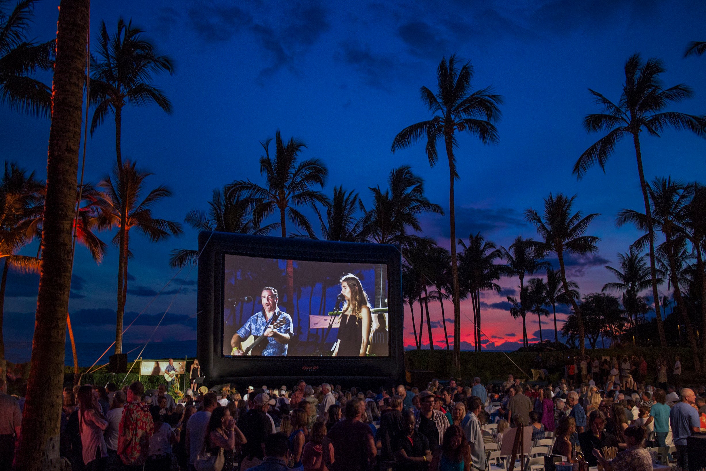 جمهور سينما في الهواء الطلق مجتمع أمام شاشة قابلة للنفخ من Open Air Cinema عند الغسق